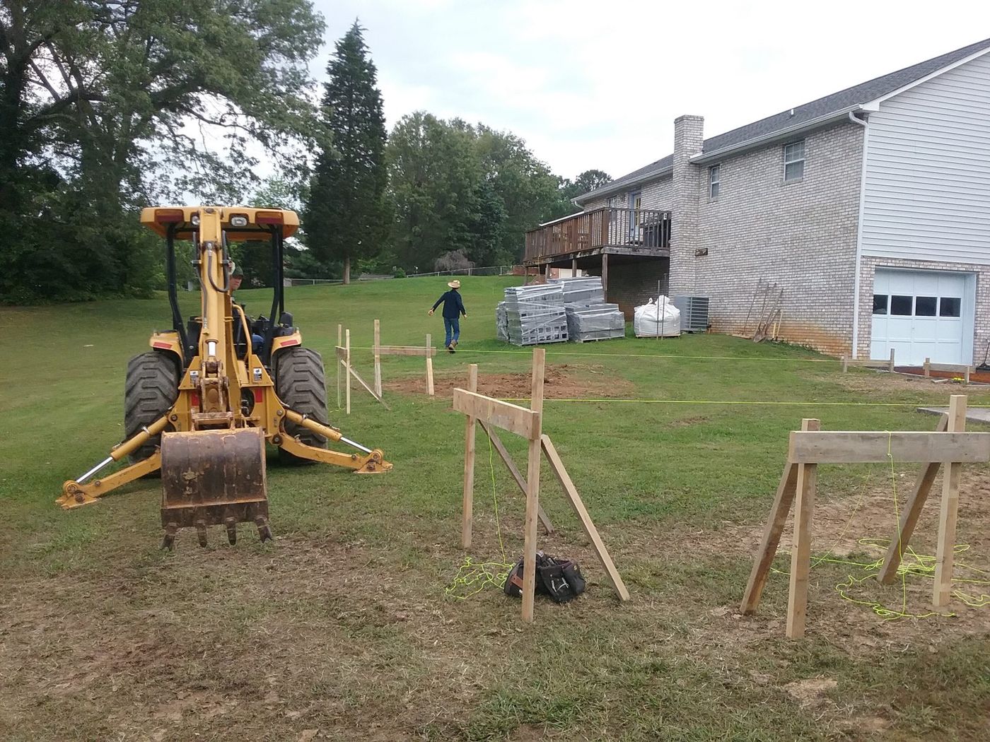 Backhoe at batter boards laid out beside a house