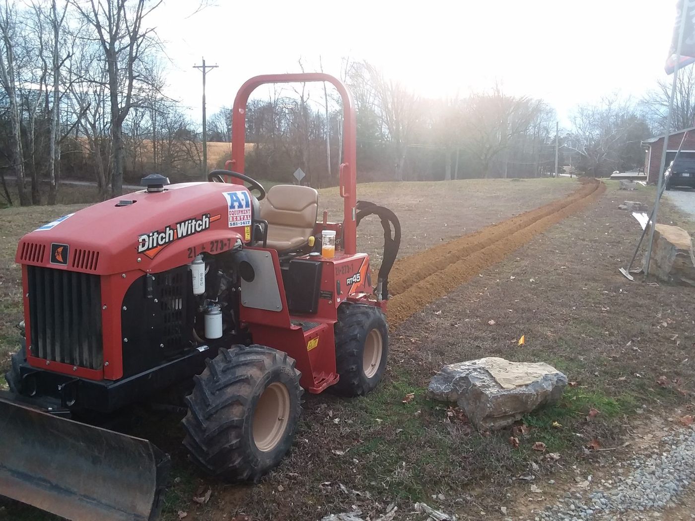 Ride-on trencher cutting a utility trench along a drive